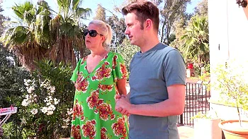 A mature woman with glasses, Maggie Moon, has fun with a young man outdoors.